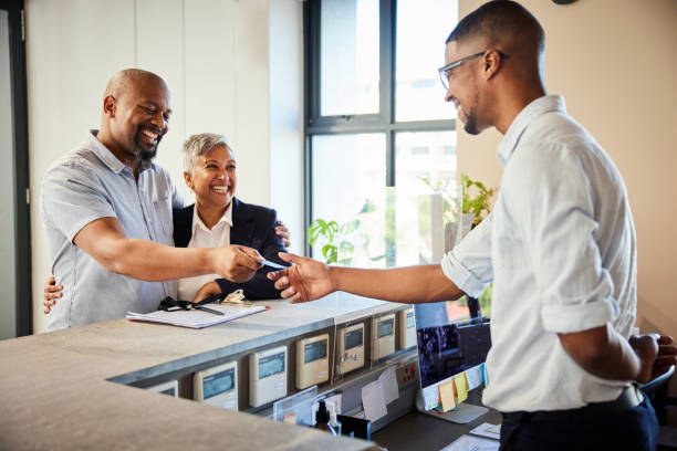 A man behind a hotel front desk hands a key card to two smiling guests.