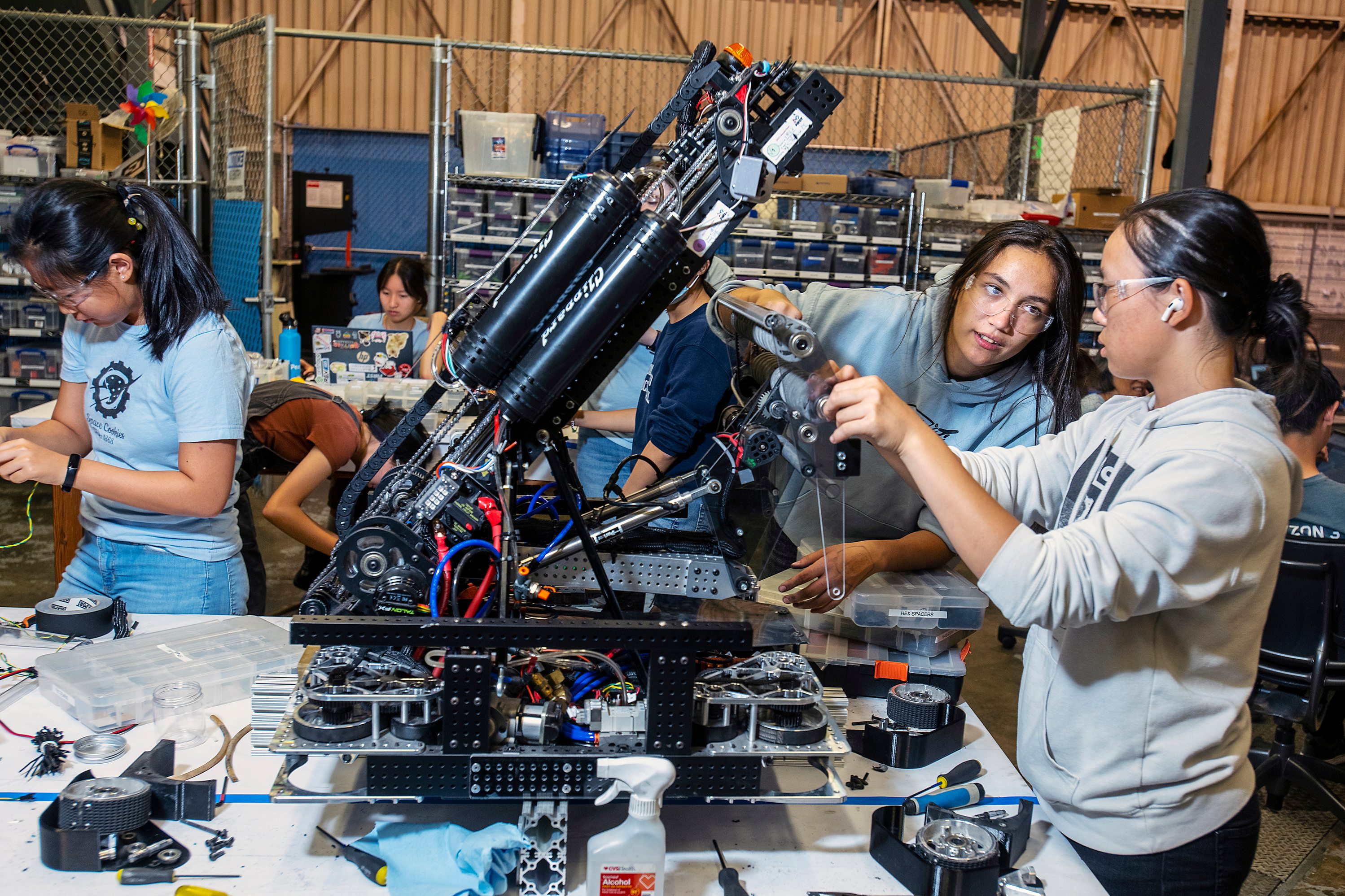 Two young women in safety glasses adjusting a robot on a workshop bench